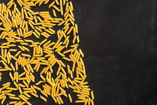 top view of raw penne pasta scattered on black background with copy space