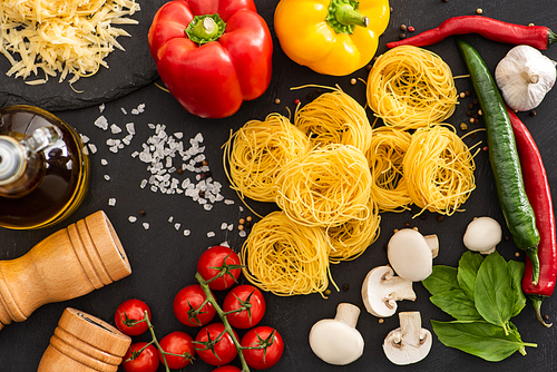 top view of raw Italian Capellini with vegetables and seasoning on black background