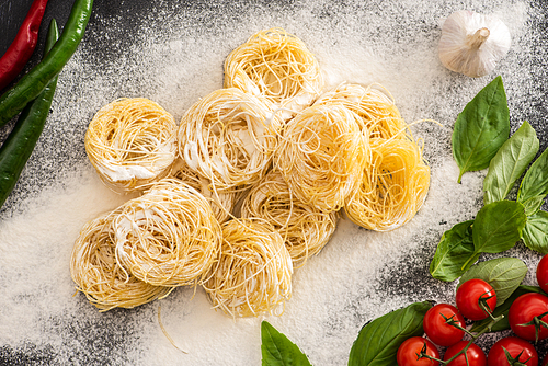 top view of raw Capellini pasta with vegetables and flour