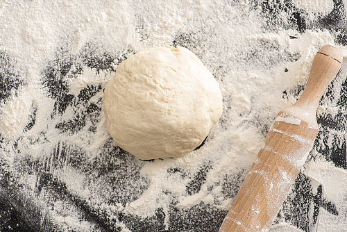 top view of rolling pin, dough on flour on black background
