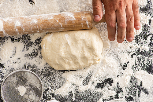 cropped view of man rolling out dough on flour on black background