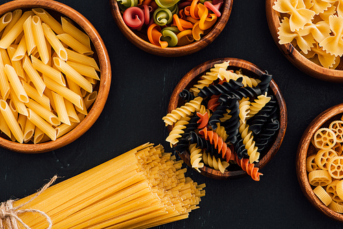 top view of assorted colorful Italian pasta in wooden bowls on black background