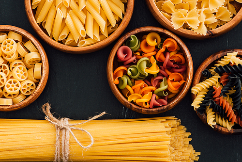 top view of assorted colorful Italian pasta in wooden bowls on black background