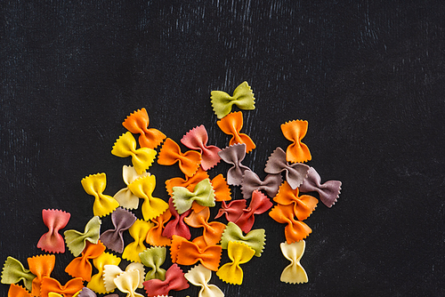 top view of colorful raw farfalle pasta on black wooden background