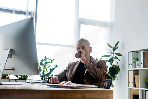 selective focus of businessman drinking coffee to go near computer monitor