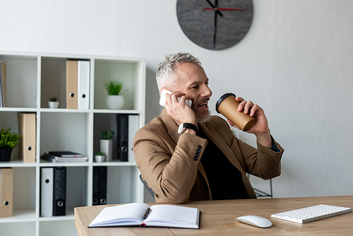 handsome businessman talking on smartphone and holding coffee to go in office