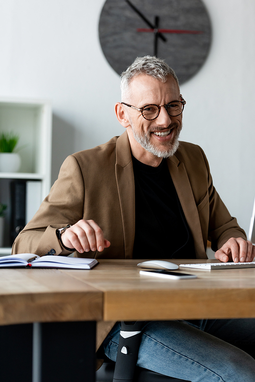 selective focus of cheerful businessman in glasses smiling in office