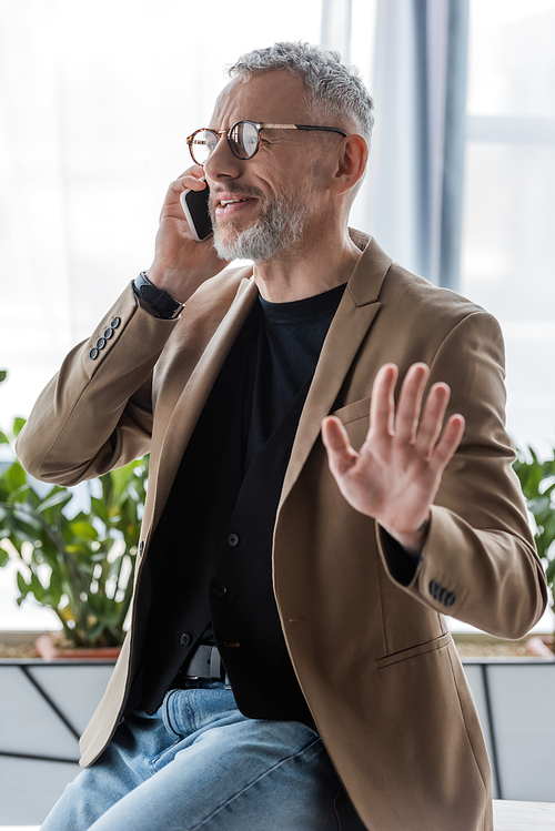 selective focus of bearded businessman in glasses gesturing and talking on smartphone