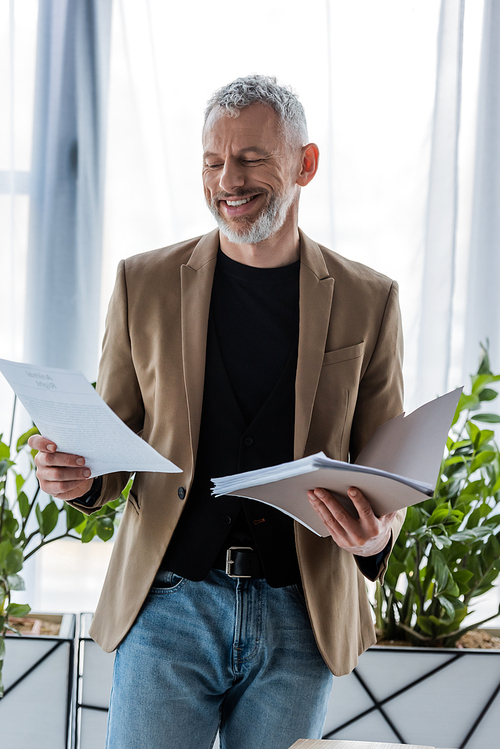 cheerful and bearded businessman looking at document while holding folder