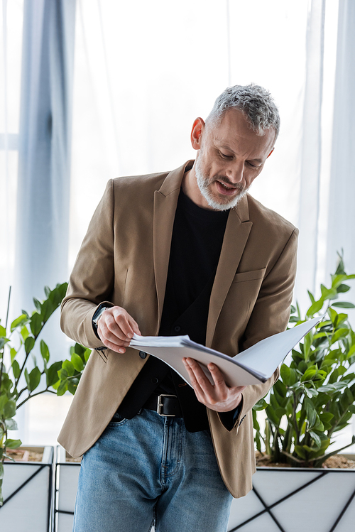 bearded businessman looking at document while holding folder in office