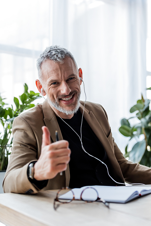 selective focus of happy businessman in earphones showing thumb up in office