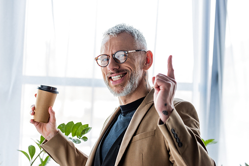 happy businessman in glasses holding paper cup and pointing with finger