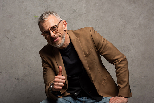 happy businessman in glasses  and showing thumb up on grey