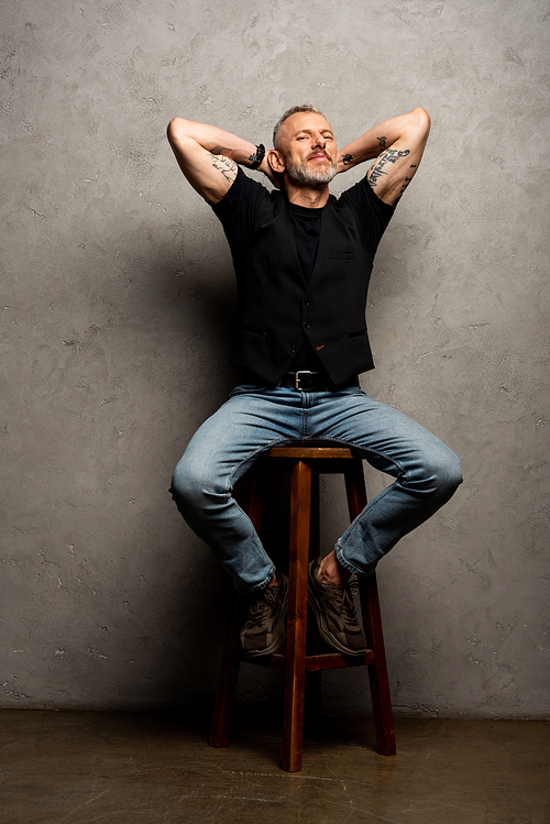 handsome man with tattoos sitting on stool on grey