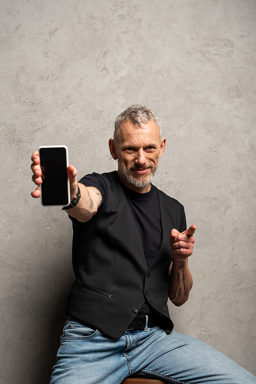 bearded man holding smartphone with blank screen and pointing with finger on grey