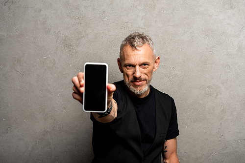 selective focus of bearded man holding smartphone with blank screen on grey