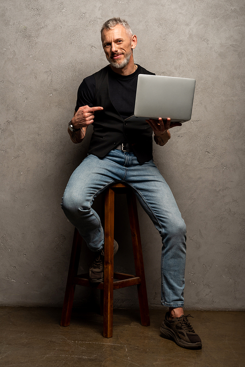 happy man pointing with finger at laptop and  on grey