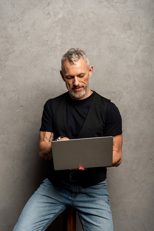handsome man with tattoo using laptop on grey