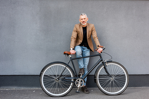 handsome businessman in blazer and jeans standing near bicycle outside