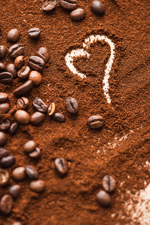 selective focus of heart drawn on ground coffee near beans