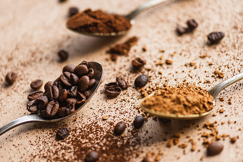 selective focus of ground, instant coffee and beans in spoons on beige surface