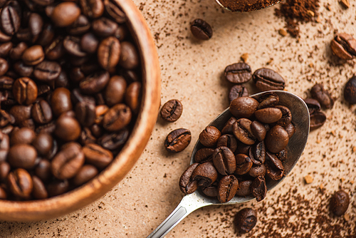 top view of coffee beans in spoon and wooden bowl on beige surface