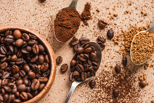 top view of ground, instant coffee and beans in spoons near wooden bowl on beige surface