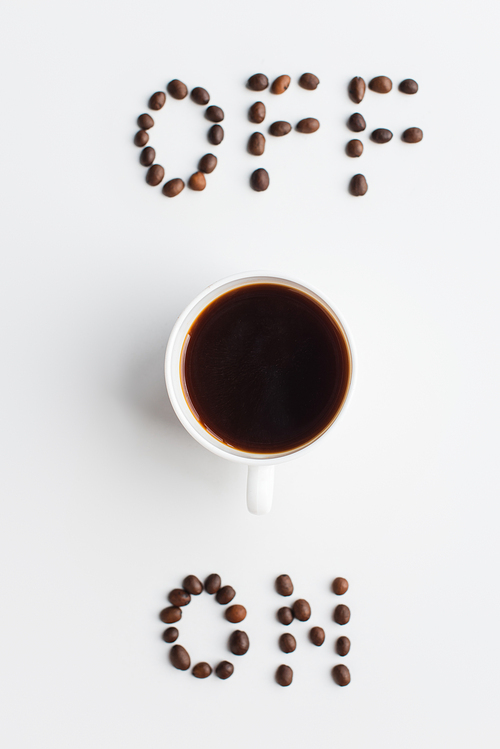 top view of on and off lettering made of coffee beans near cup on white surface