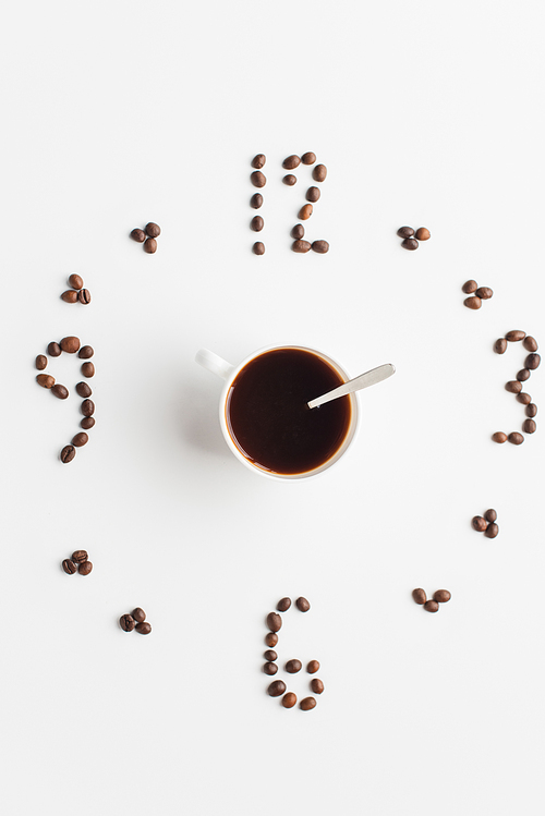 top view of clock made of coffee beans around cup on white surface