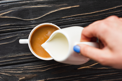 cropped view of barista adding milk to coffee in cup on wooden surface