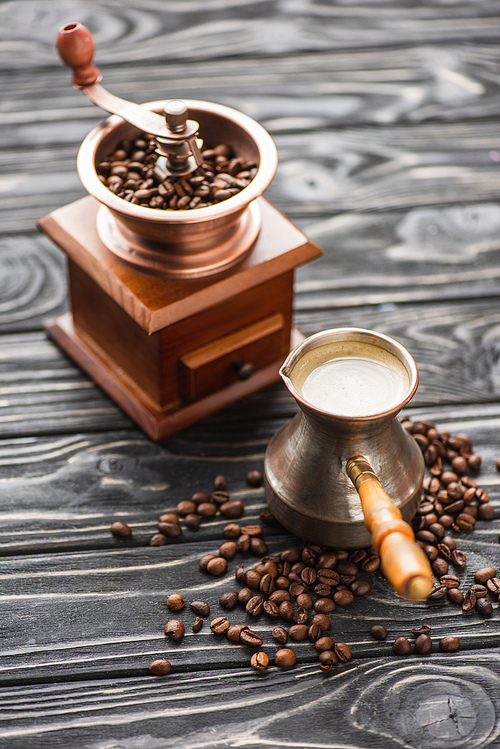 selective focus of vintage coffee grinder with coffee beans near cezve on wooden surface