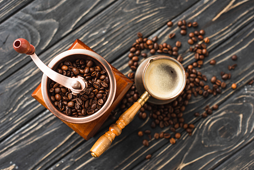 top view of vintage coffee grinder with coffee beans near cezve on wooden surface