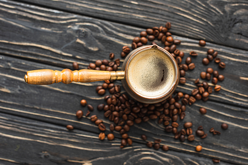 top view of cezve with coffee on coffee beans on wooden surface