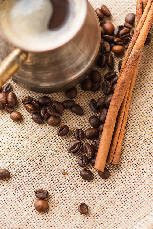 close up view of cezve with coffee near cinnamon sticks and coffee beans on sackcloth