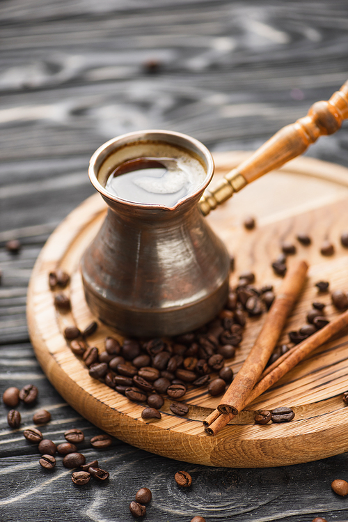 selective focus of cezve with coffee near cinnamon sticks on wooden board