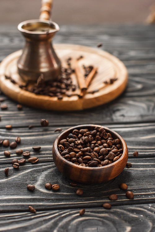 selective focus of coffee beans in bowl and cezve on wooden surface