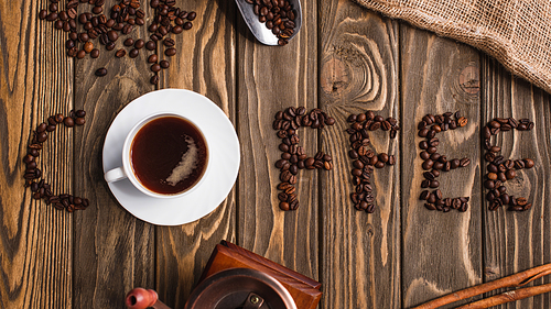 top view of cup of coffee on saucer and coffee lettering made of beans on wooden surface