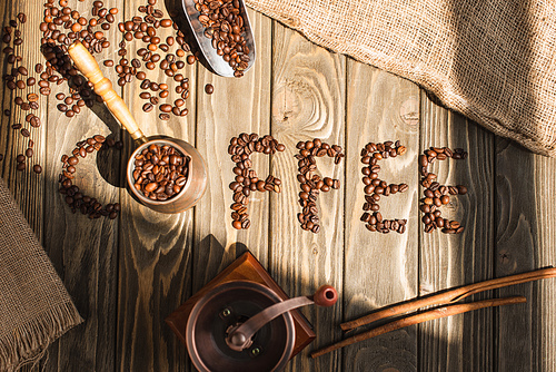 top view of coffee lettering made of beans and coffee grinder with cezve in sunlight on wooden surface