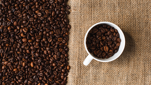 top view of cup with coffee beans and sackcloth on background