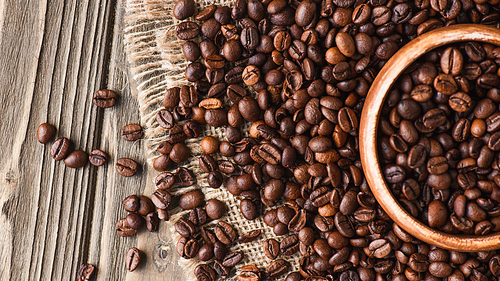 top view of coffee beans scattered on burlap from bowl on wooden surface