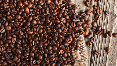 top view of coffee beans scattered on burlap on wooden surface