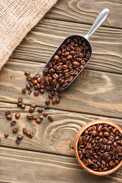 top view of sackcloth, metal scoop with coffee beans and bowl on wooden surface