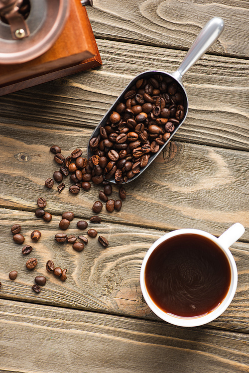 top view of vintage coffee grinder, metal scoop with coffee beans and cup on wooden surface