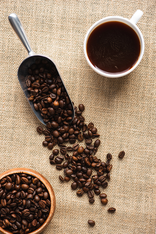 top view of cup, metal scoop with coffee beans and bowl on sackcloth