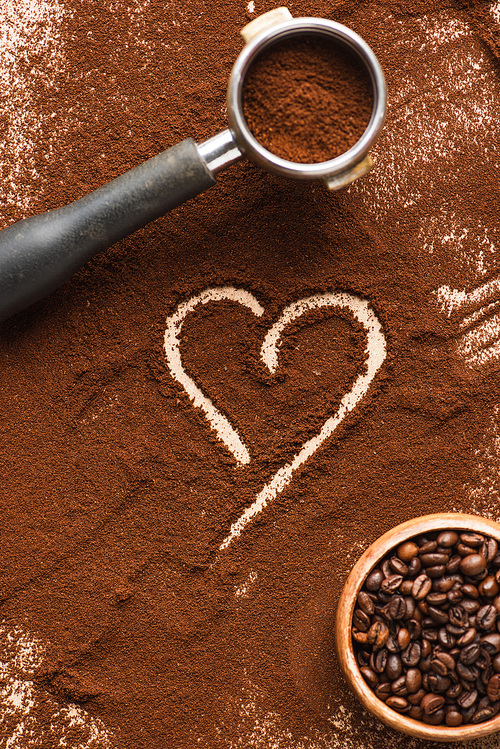 top view of heart drawn on ground coffee near beans in bowl and portafilter