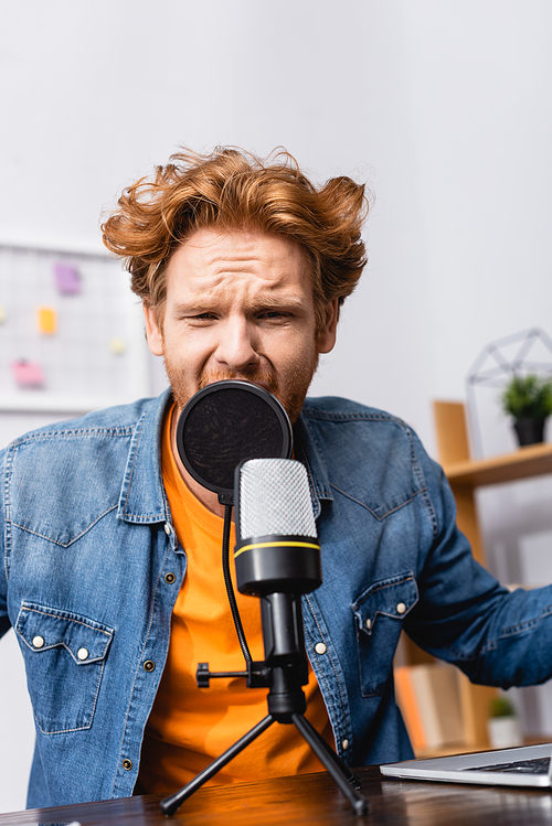 tense redhead announcer in denim shirt speaking in microphone at workplace