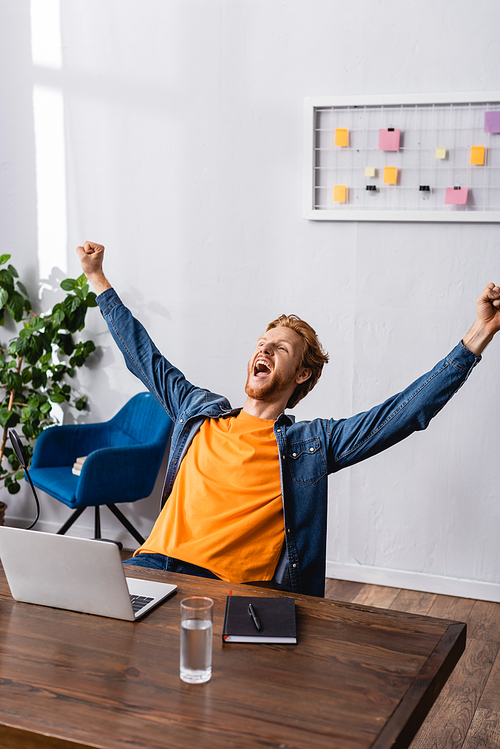 excited radio host in denim shirt showing winner gesture and screaming near microphone and laptop