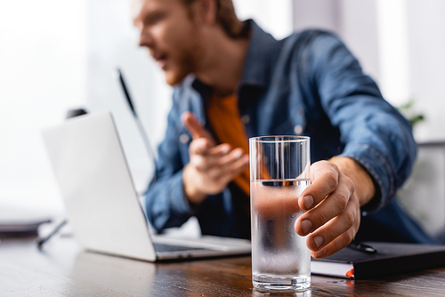 selective focus of announcer taking glass of cold water while speaking in microphone