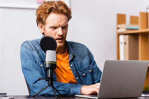 concentrated redhead radio host using laptop while sitting near microphone