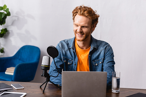redhead broadcaster in denim shirt working near microphone and laptop